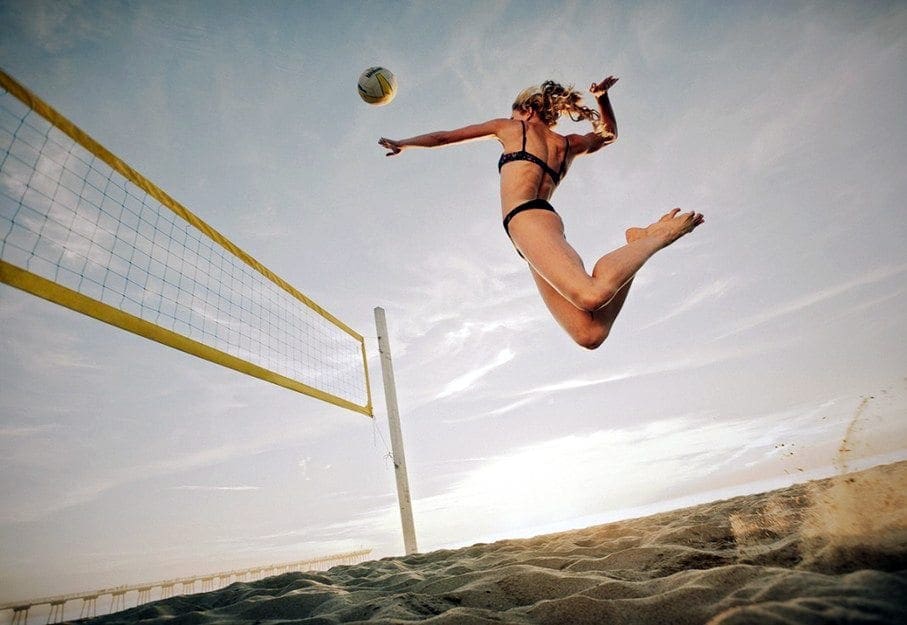 blog picture of lady playing beach volleyball jumping high for a spike