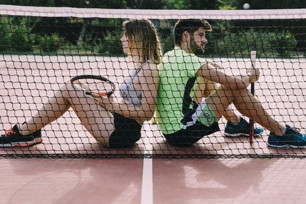 giocatori di gomito del tennista che prendono pausa seduti vicino alla rete