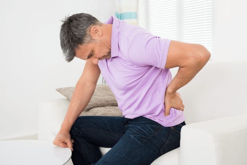 Immagine di un uomo che si tiene la schiena a causa della sciatica e del dolore radicolare alla schiena e alle gambe.